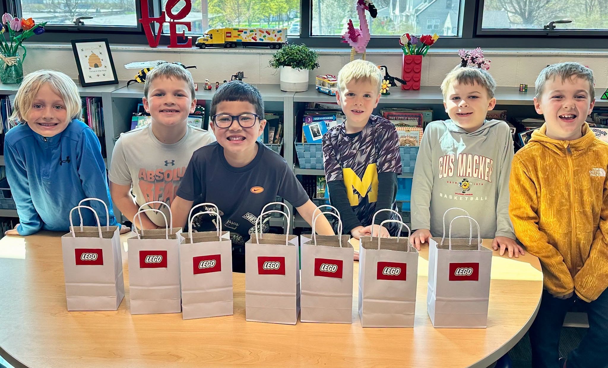 Six elementary students at a library table lined with LEGO gift bags