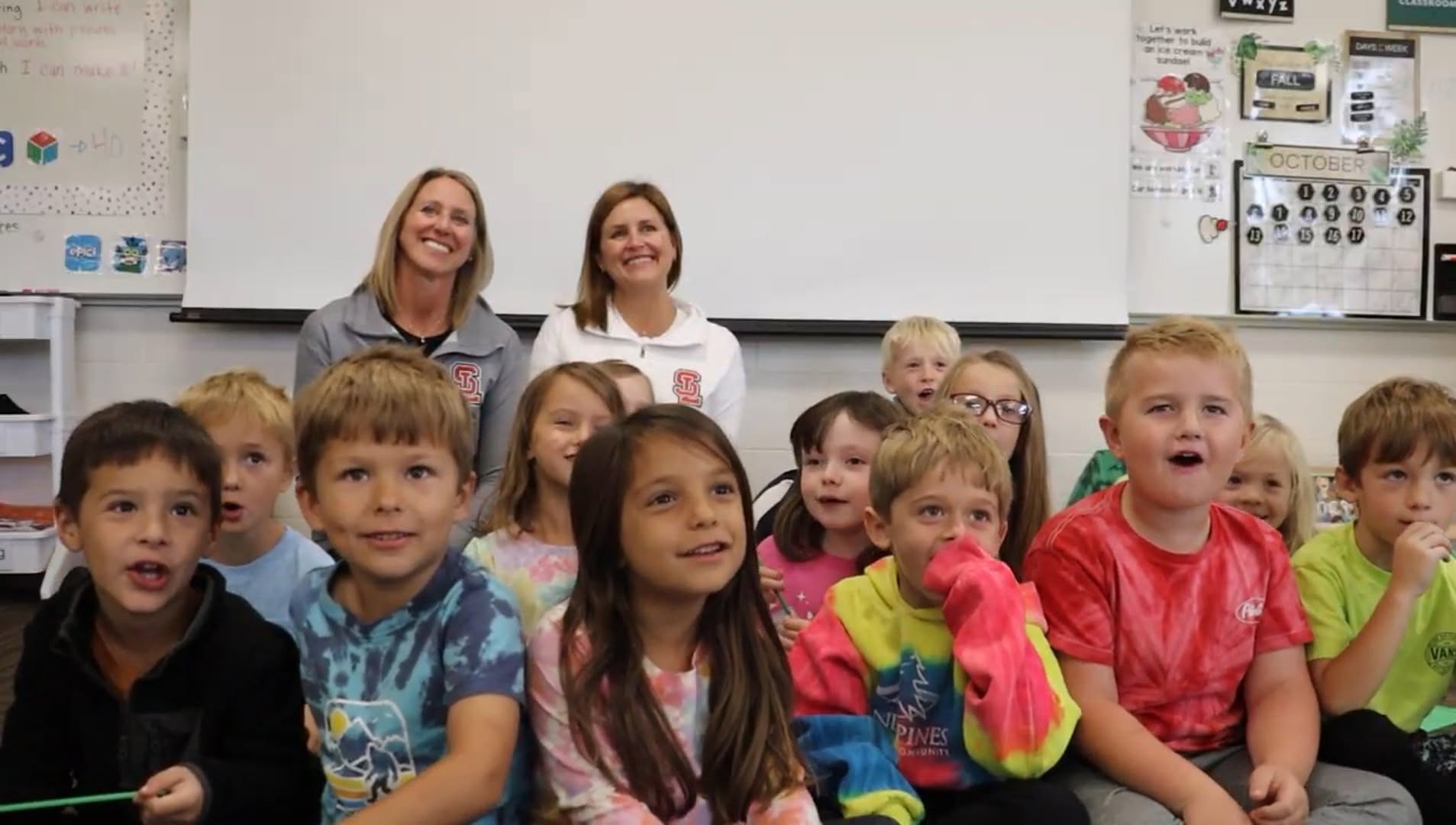Two staff members with a kindergarten class seated together on the classroom floor