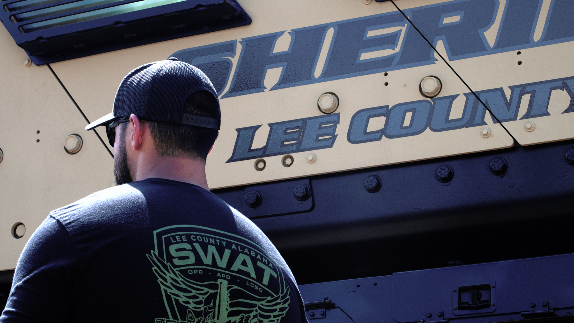 Team member in a Lee County Alabama SWAT shirt beside the Sheriff's armored vehicle