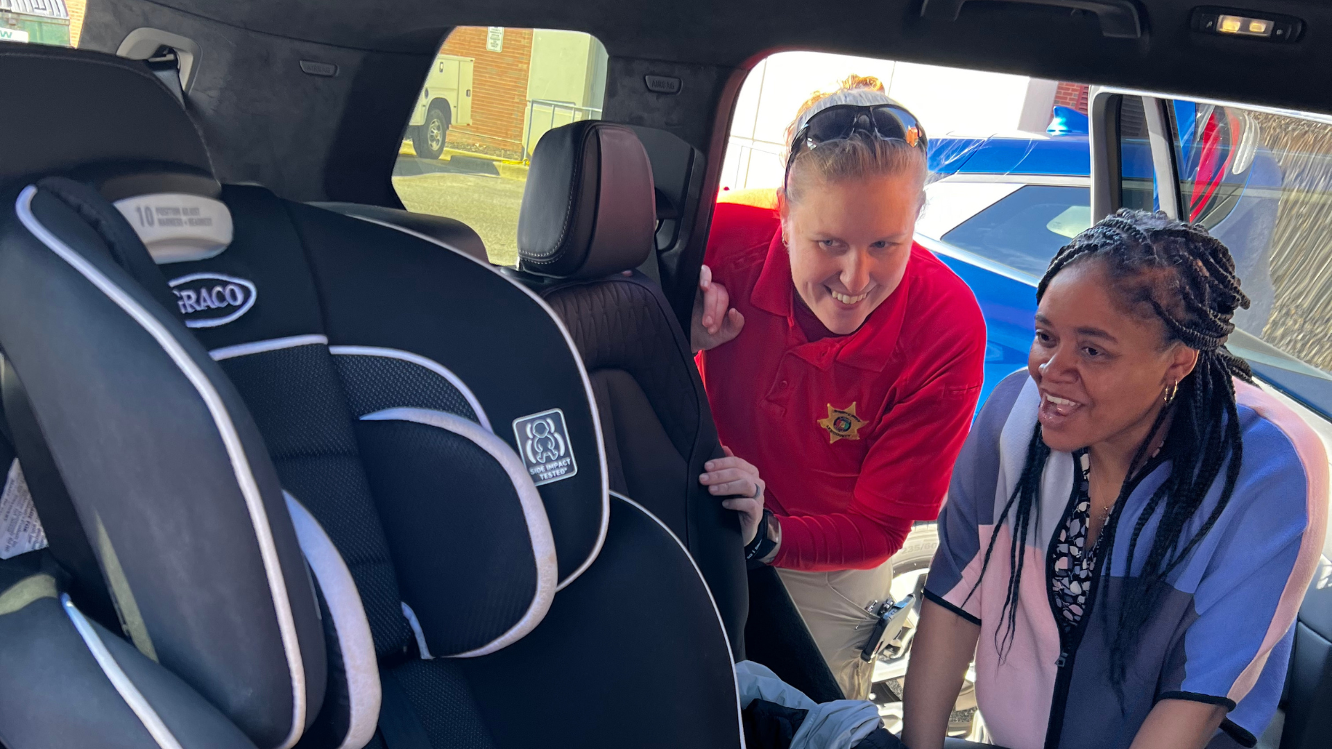 two women smiling looking at a carseat in the backseat of a car